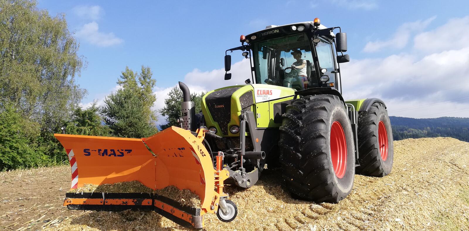Claas Xerion mit Schubschild verteilt Hackschnitzel auf dem Lagerplatz, im Hintergrund Nadelwald