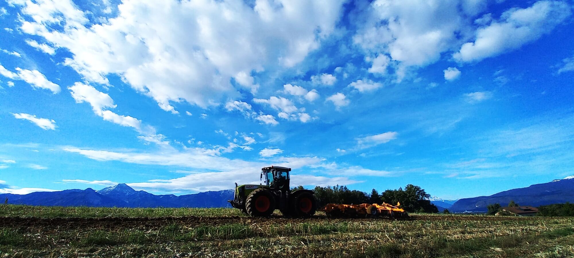 Claas Xerion Traktor bei der Bodenbearbeitung mit Grubber, unter dramatischem Wolkenhimmel vor der Bergkulisse der Karawanken in Kärnten